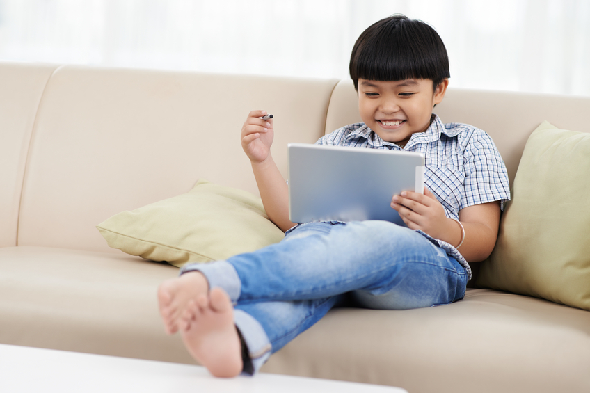Portrait of cute little boy playing on tablet computer at home