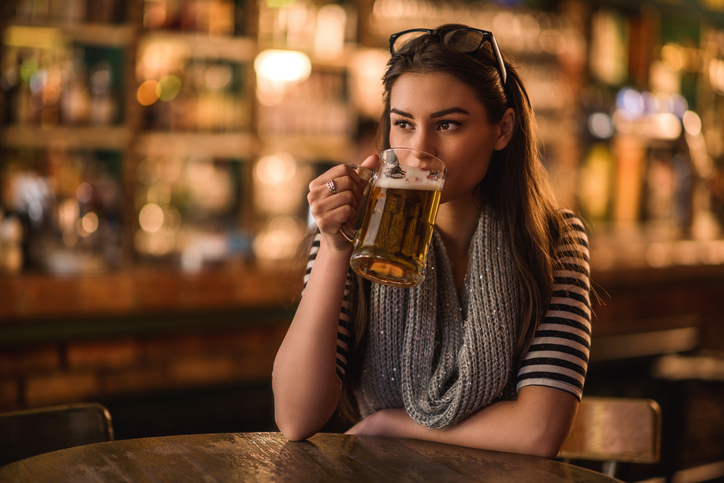 Beautiful young woman drinking beer while sitting alone in a cafe. She is looking away.